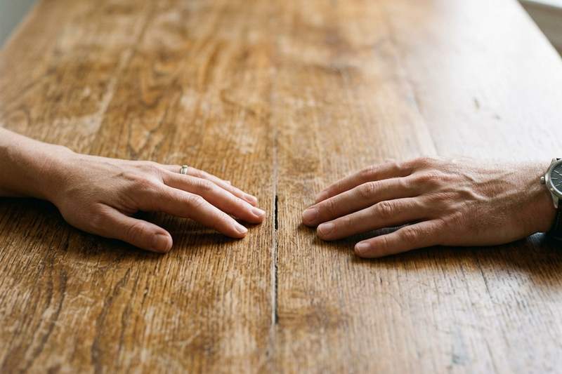 Close-up of a woman's hands resting on a wooden table, representing the space and emotional tension between partners during de-escalation exercises